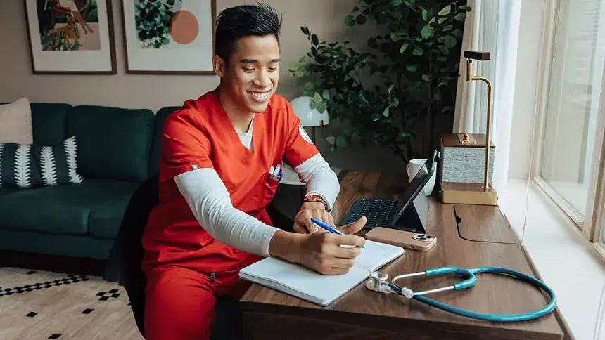 Man in scrubs at a desk in a furnished apartment